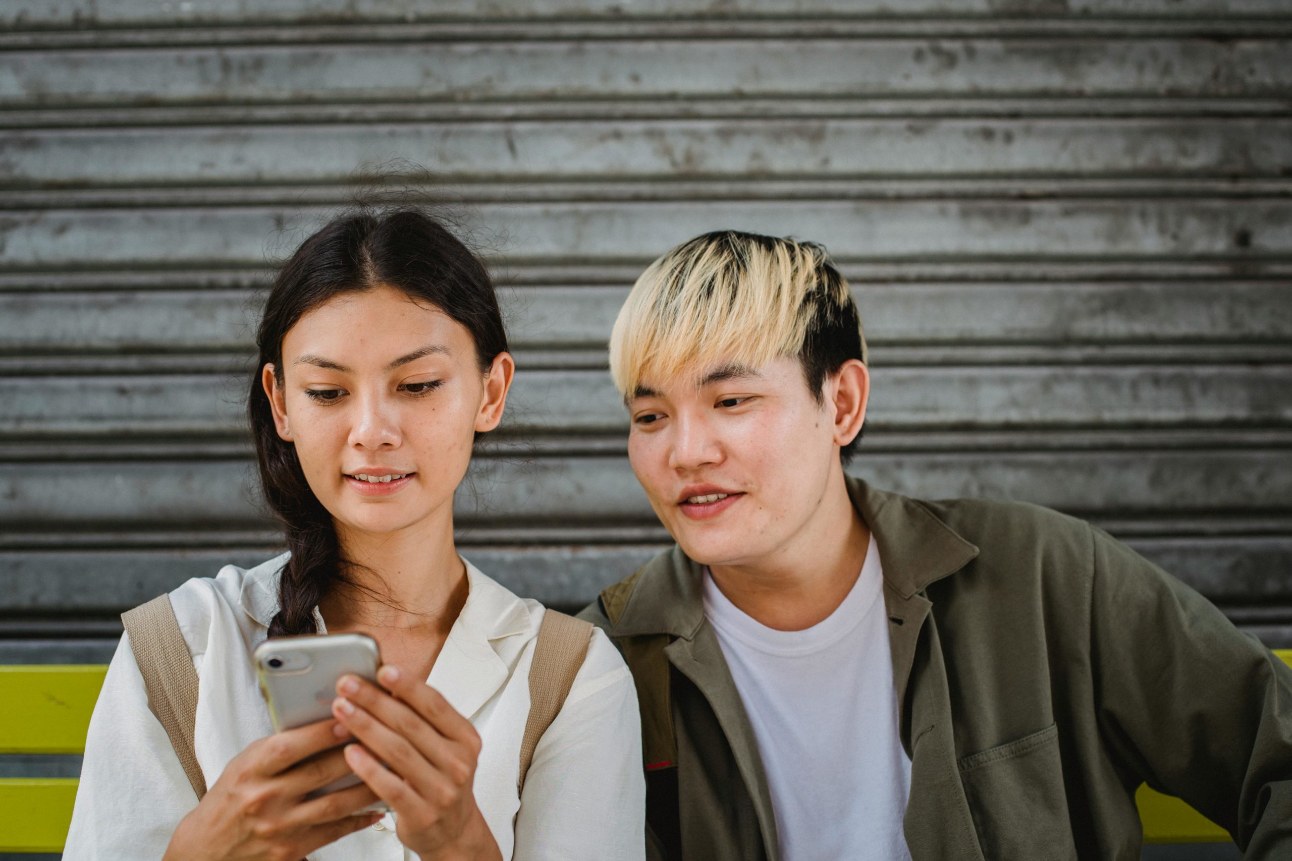 Fröhliches Asiatisches Paar, Das Smartphone Auf Straßenbank Durchsucht